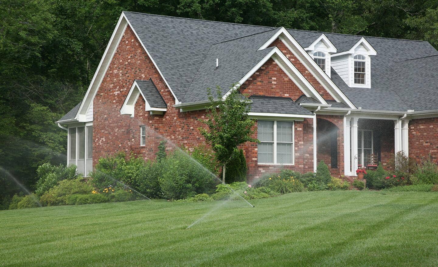 Sprinklers watering a healthy green lawn in front of a brick house