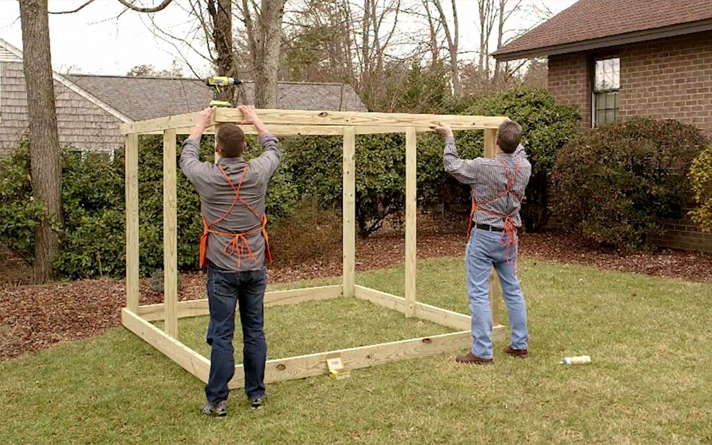 Two workers attach a wooden stud to the top of a garden enclosure frame. Two workers attach a wooden stud to the top of a garden enclosure frame.