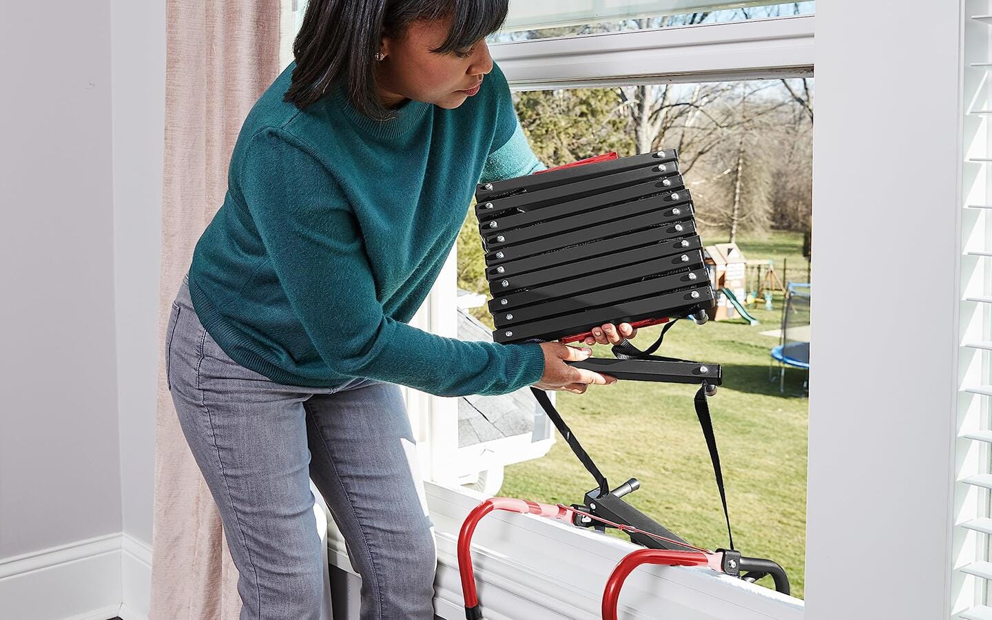 A woman prepares to drop a fire escape ladder from a window.