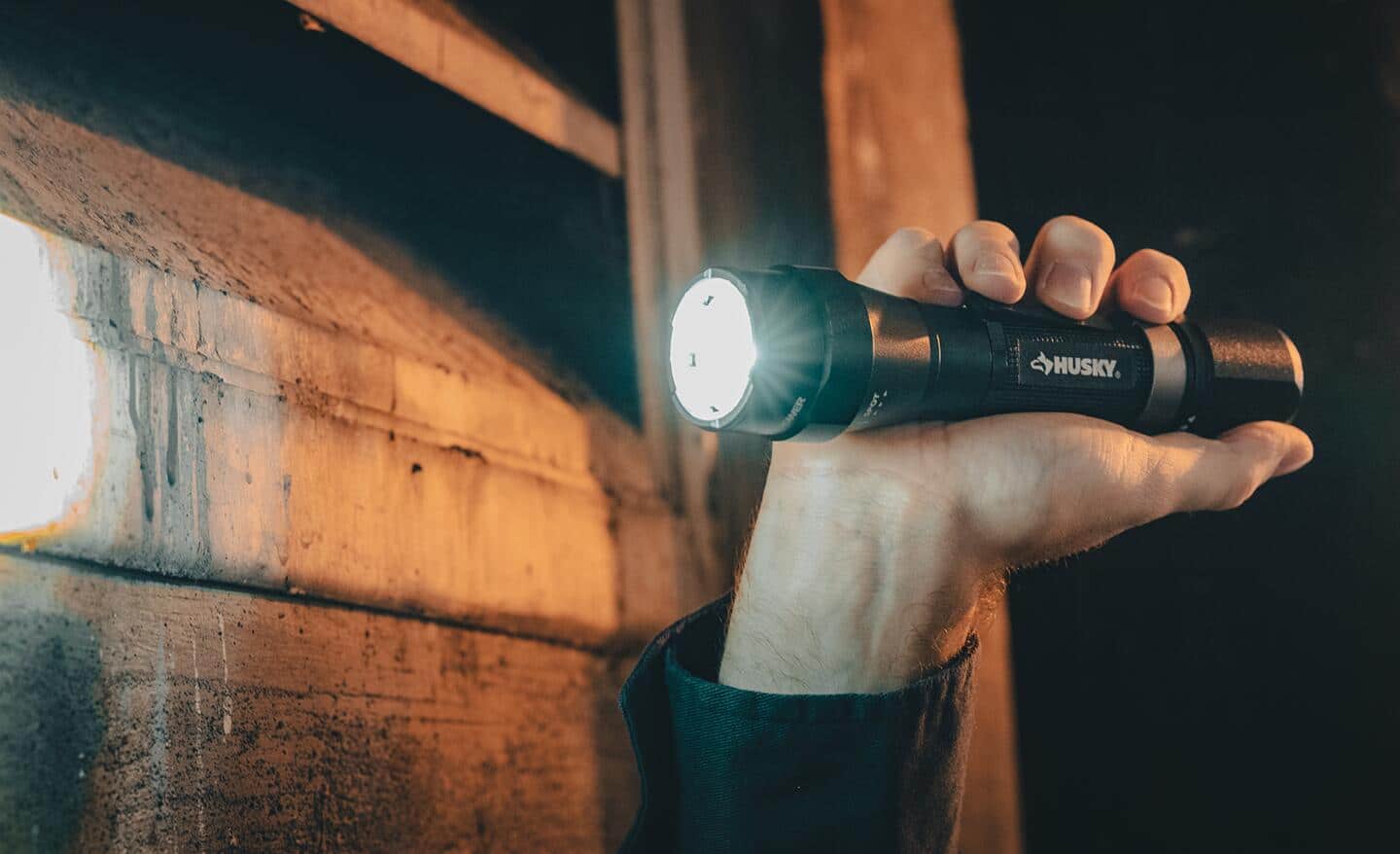 A person holds a black flashlight, shining it onto lumber on a wall.