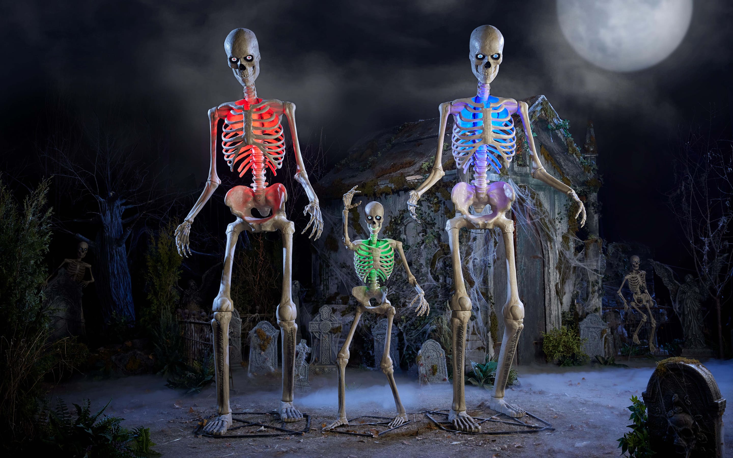 A pair of 12-foot skeletons posed with a 6-foot skeleton in a spooky scene.