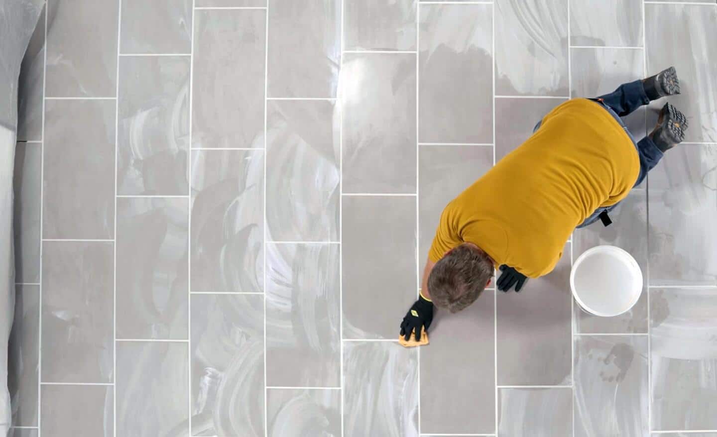 Person uses a damp cloth to wipe freshly grouted tile floor 