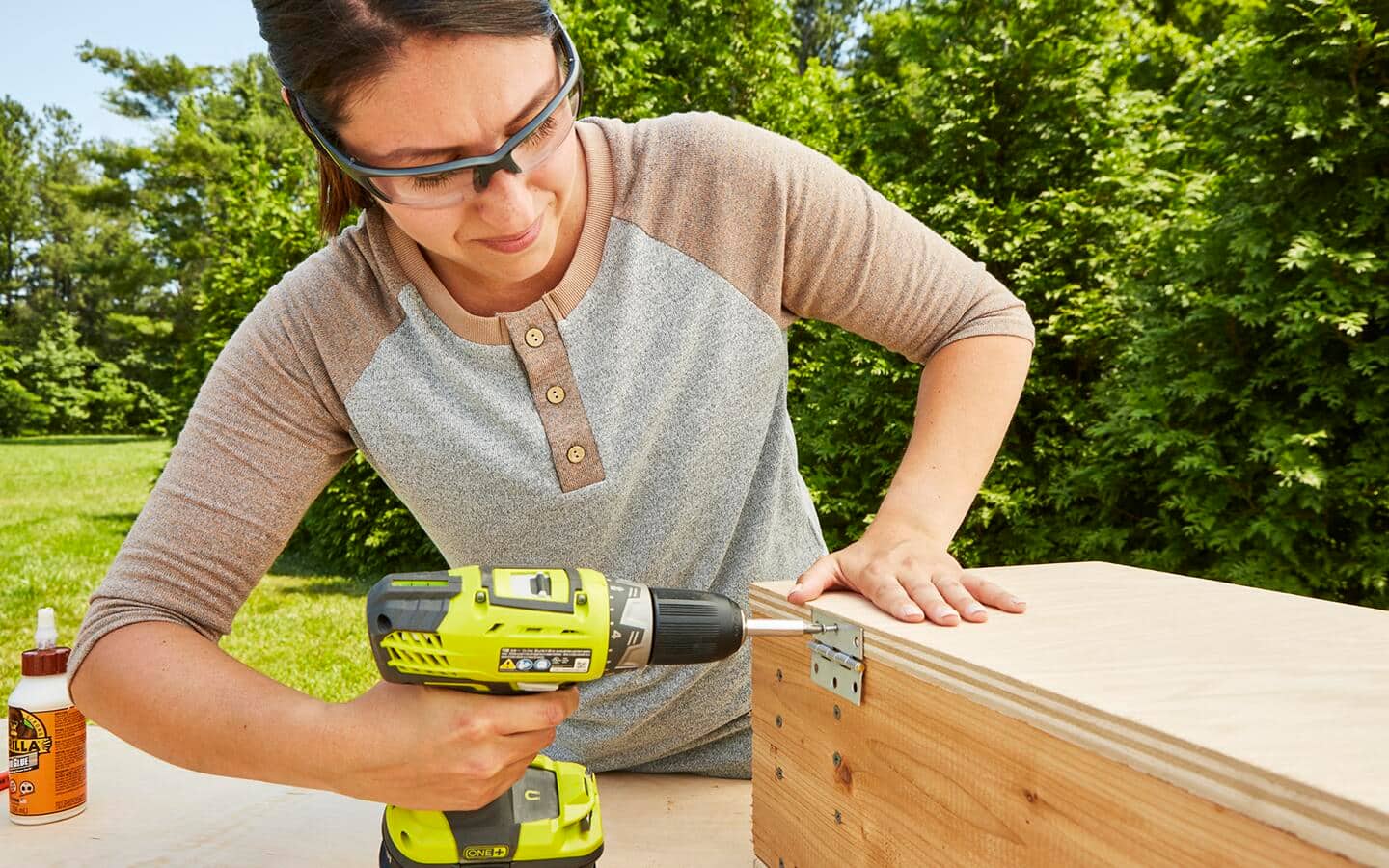 A person uses a drill to attach a hinge to the root cellar box lid. A person uses a drill to attach a hinge to the root cellar box lid.