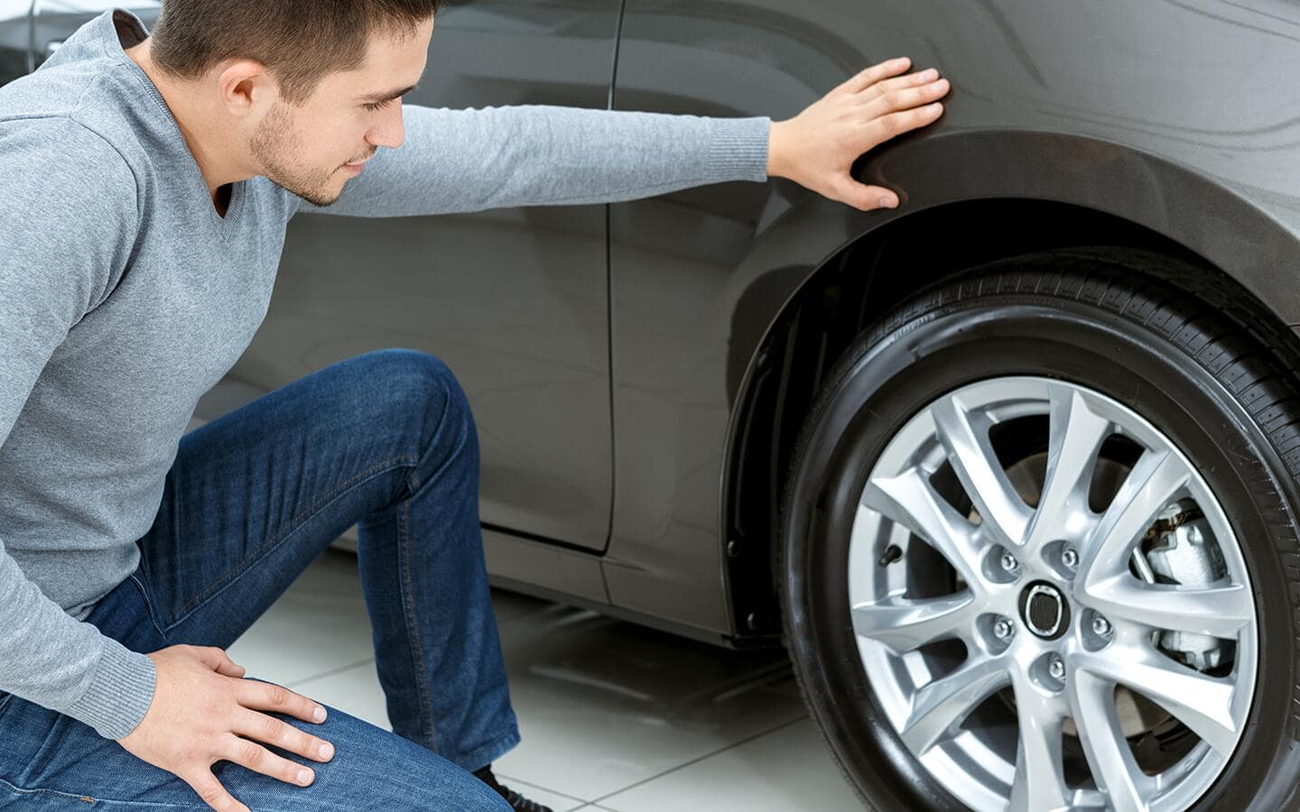A man examines one of the tires on a car.