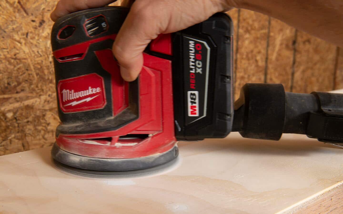 A battery powered random orbital sander is used to smooth the surface of plywood and wood filler.