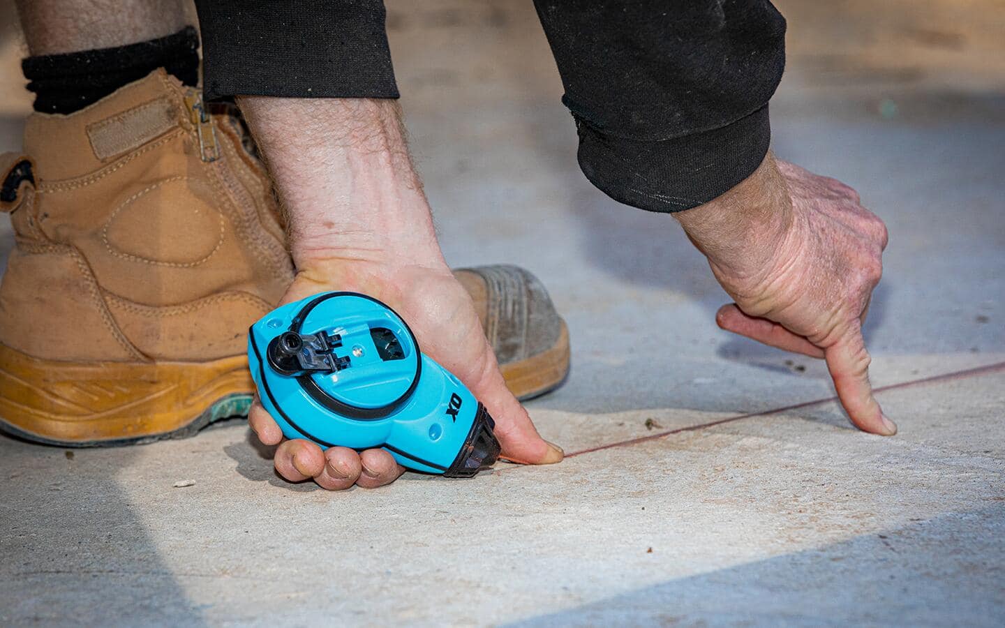 A person uses a chalk line to make a mark on a floor before installing parquet tile. A person uses a chalk line to make a mark on a floor before installing parquet tile.