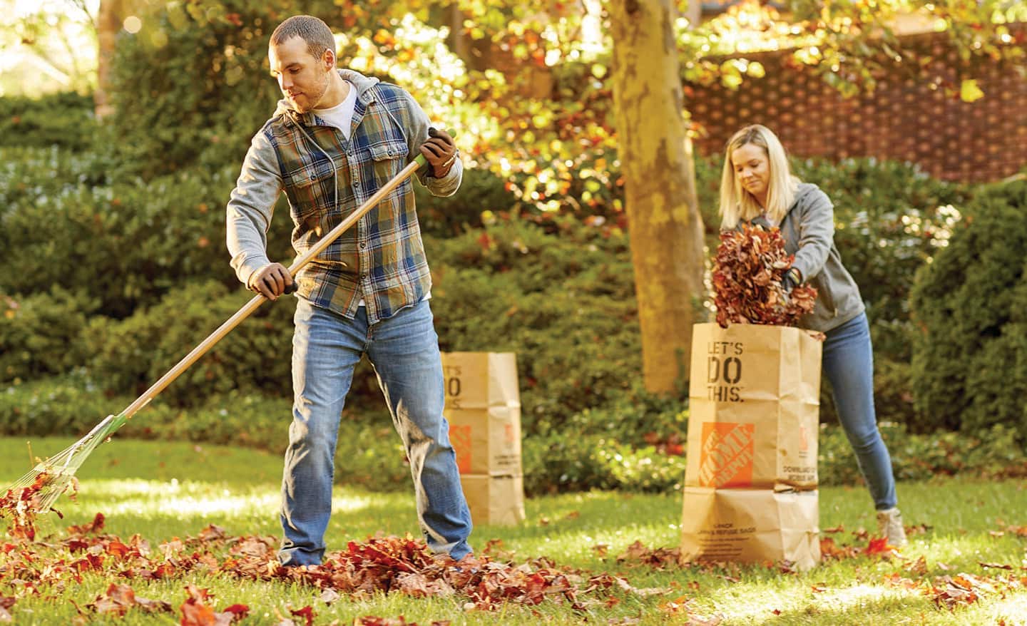 Two people rake leaves and place them in brown paper leaf bags