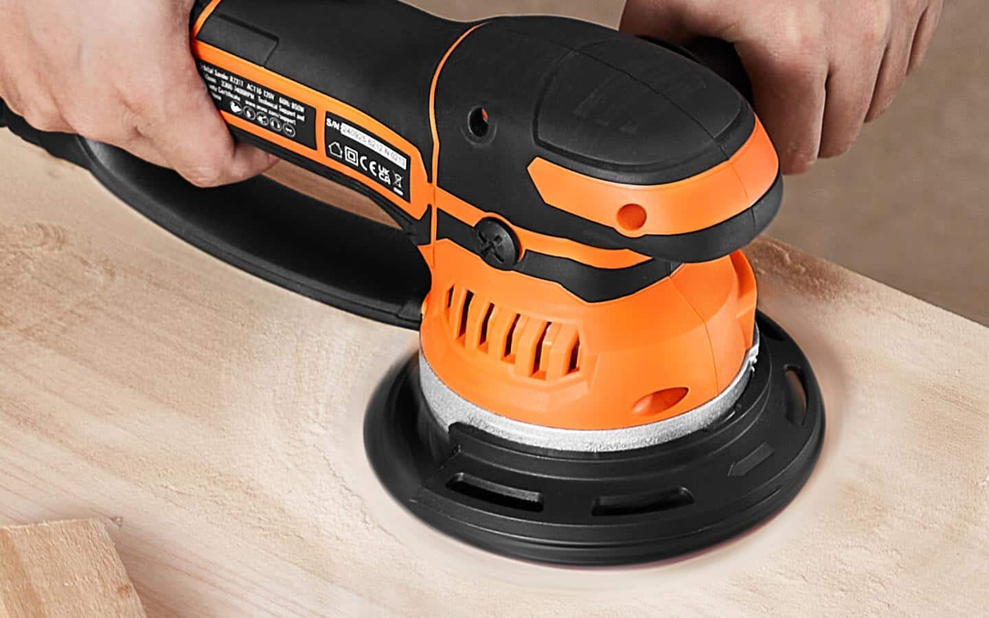 A person sanding a wood wall shelf with an orange orbital sander.