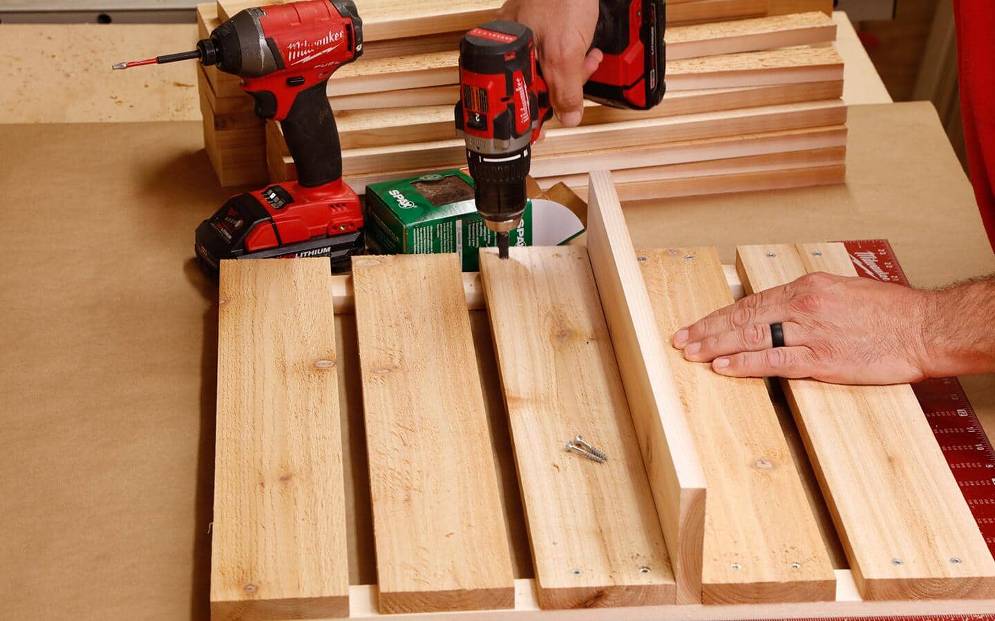 Someone drilling cedar boards together to construct a compost bin's side.