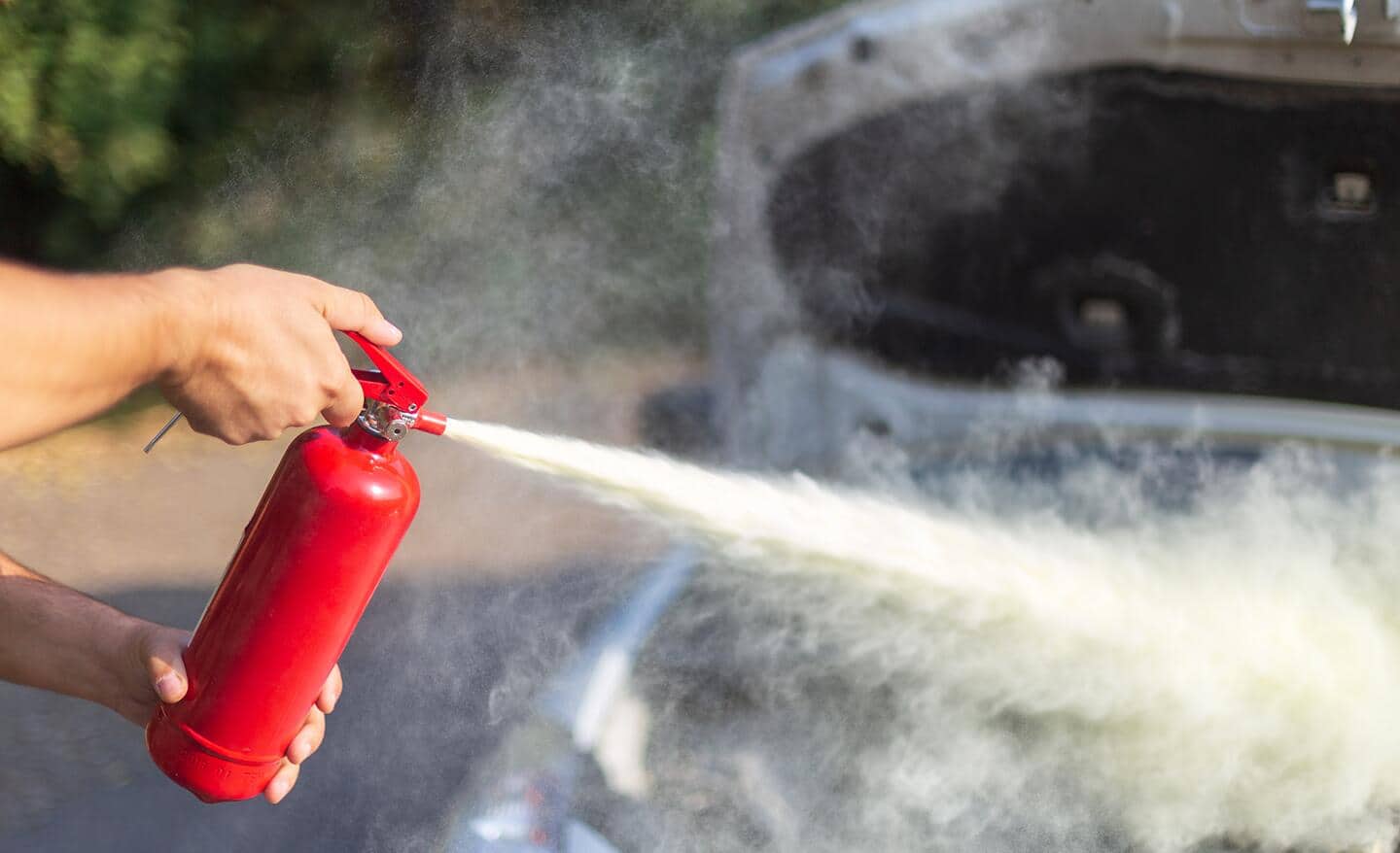 Someone using a fire extinguisher to put out an car engine fire.
