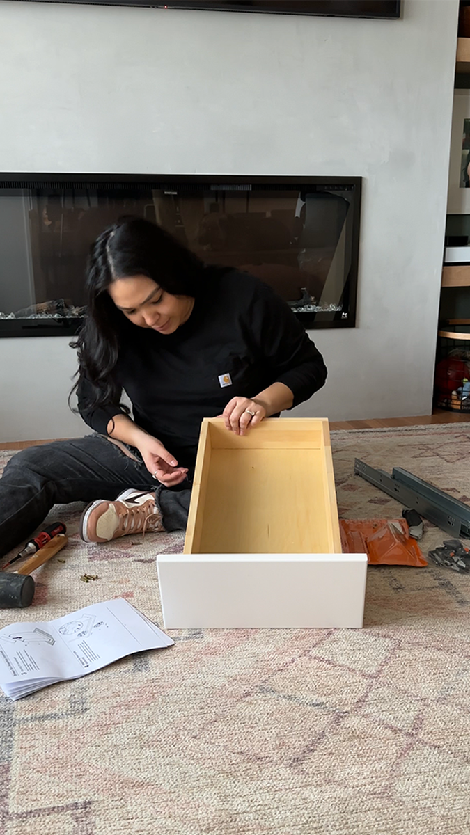 Vanessa sits on the floor while she assembles a cabinet drawer to use in her kitchen transformation.