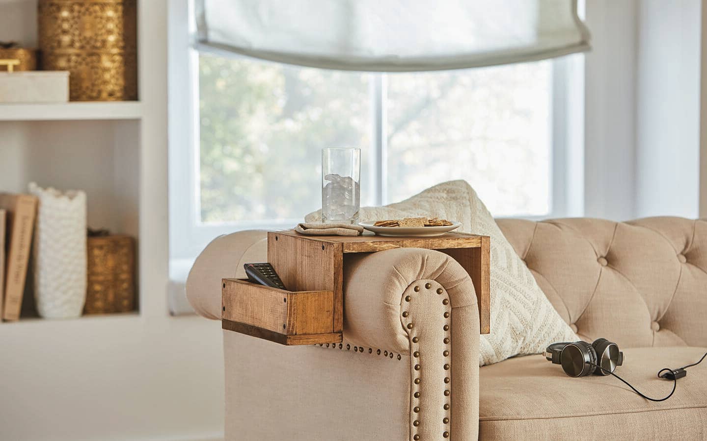 A completed sofa table on a couch's arm with a glass, plate and other items.