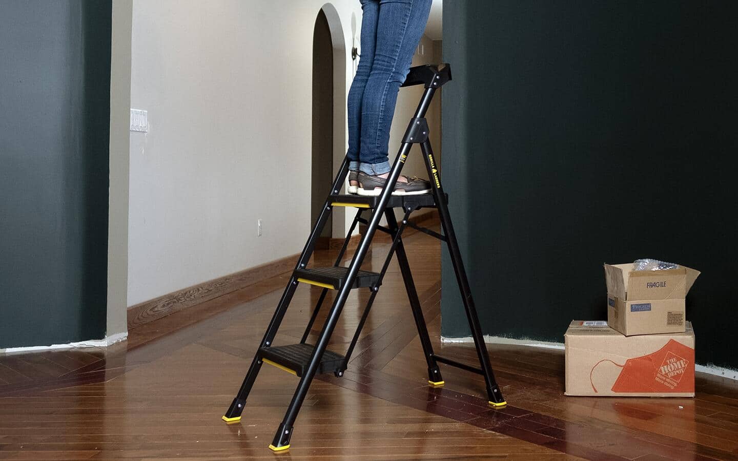 A person stands on a step stool that is set up on a hardwood floor. A person stands on a step stool that is set up on a hardwood floor.