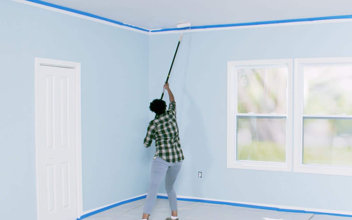 A person uses an extension pole and roller to paint a room's ceiling. A person uses an extension pole and roller to paint a room's ceiling.