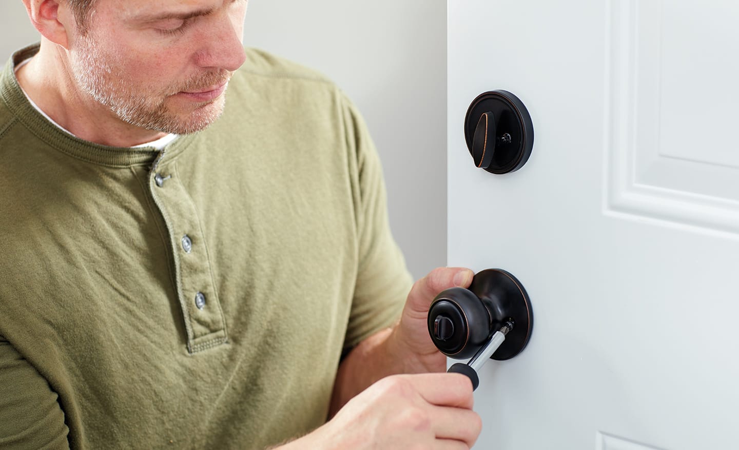 A man installing a door knob and safety lock on a new entry door.