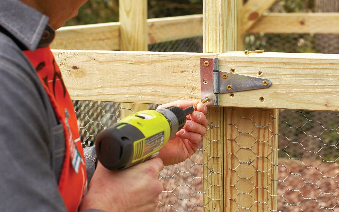 A person drills in steel hinges to complete the door of garden enclosure. A person drills in steel hinges to complete the door of garden enclosure.