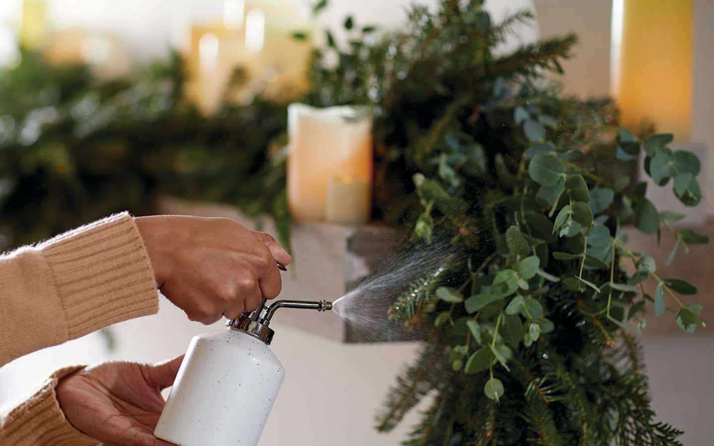 A person spritzes fresh greenery with water from a white dispenser.