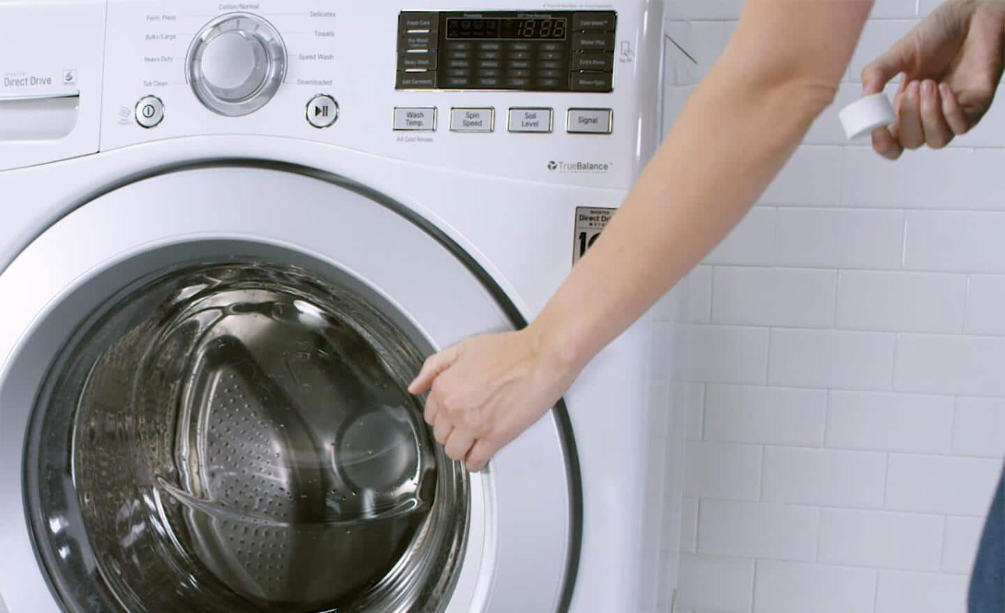 A person about to toss a cleaning tab into a front load washer tub.