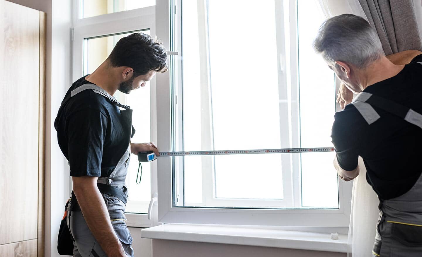Two people measure a window's exterior.