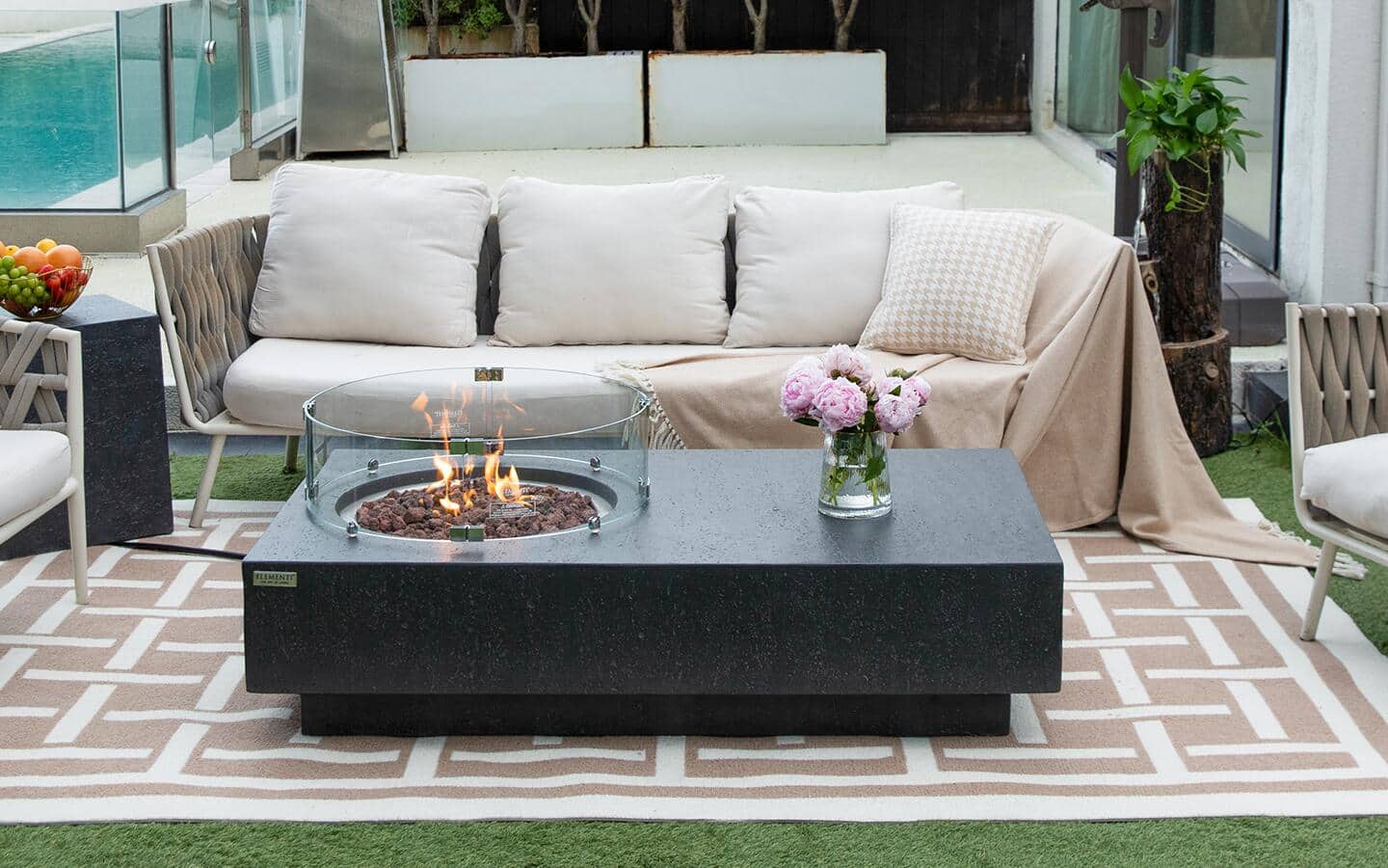 A granite and glass fire pit table on a rug with patio furniture.
