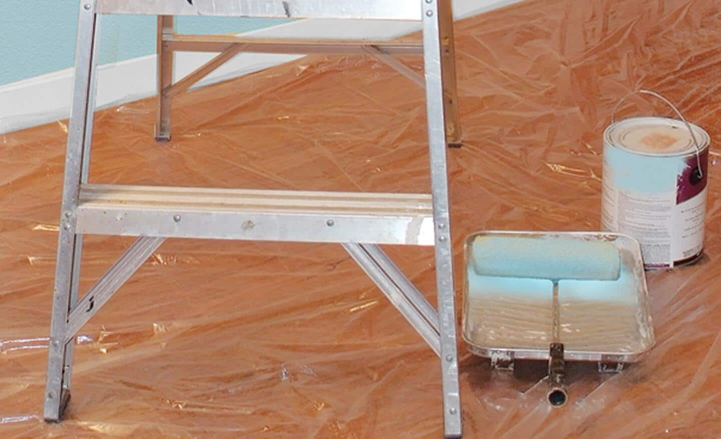 Plastic sheeting, with a ladder, paint can and paint accessories on it, covers a floor.