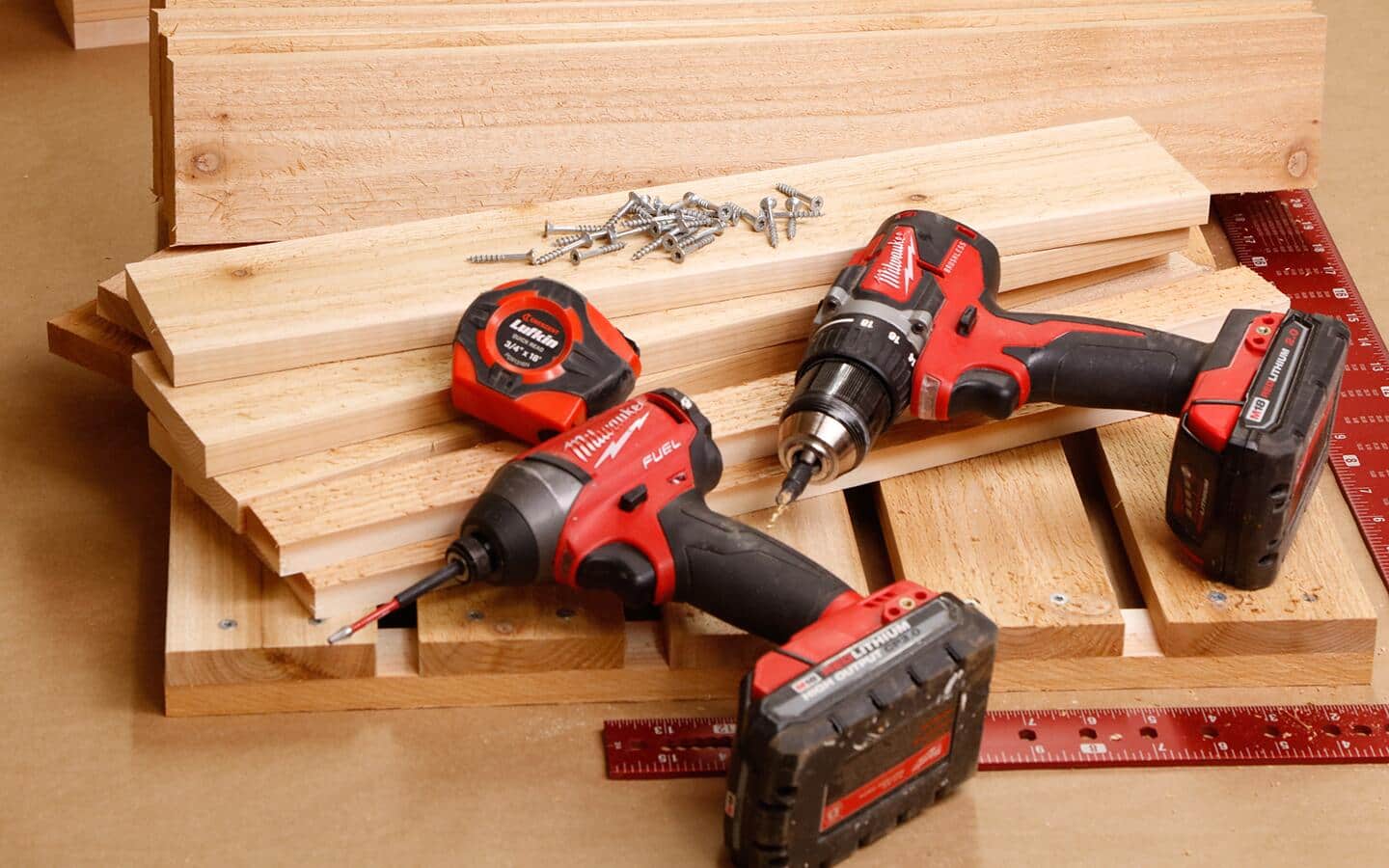 A pair of cordless drills, screws and a ruler placed on wood boards.
