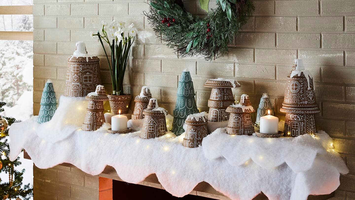 A holiday mantle featuring a gingerbread village made from terra cotta pots and saucers.