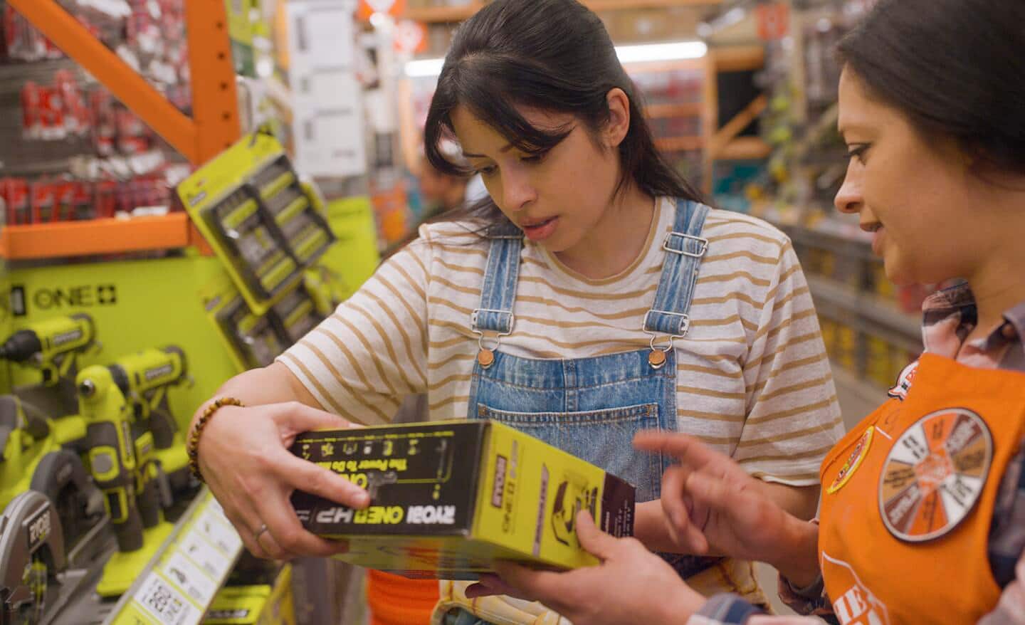 Home Depot employee shares a Ryobi power tool battery product with an inquiring customer.