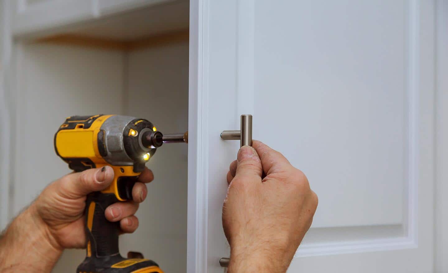 A person attaches a handle to a cabinet door.
