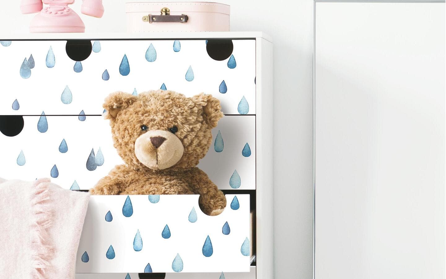 A toy bear stuffed into a dresser drawer wallpapered in blue raindrops. A toy bear stuffed into a dresser drawer wallpapered in blue raindrops.