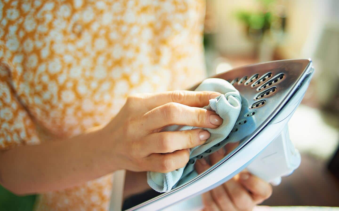 A person cleaning a dry iron's soleplate. A person cleaning a dry iron's soleplate.