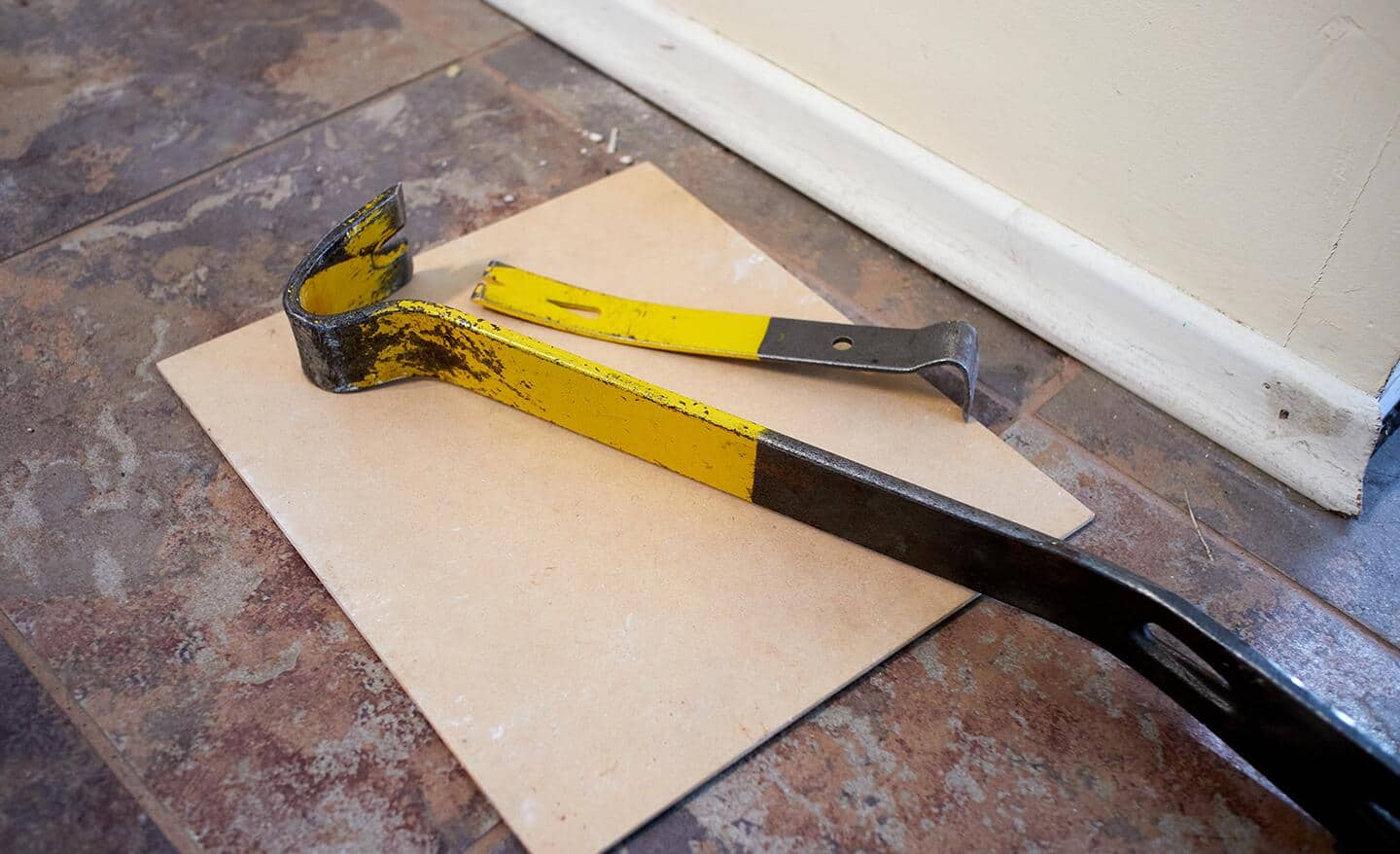 A yellow pry bar placed on top of a baseboard.