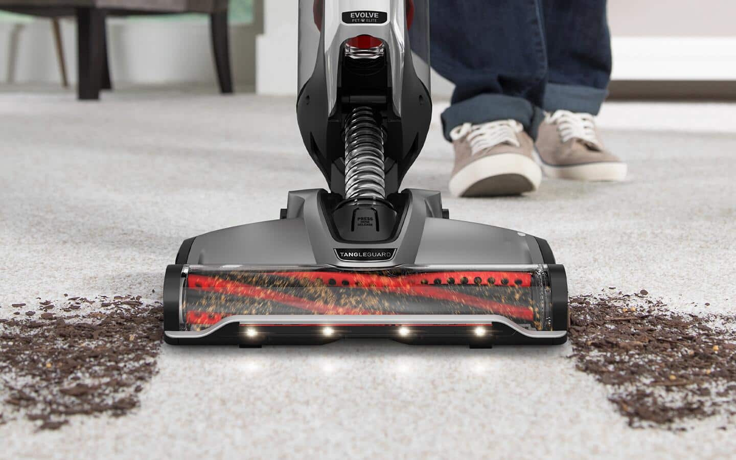 Someone using a powerful vacuum to get the dirt out of a gray carpet.