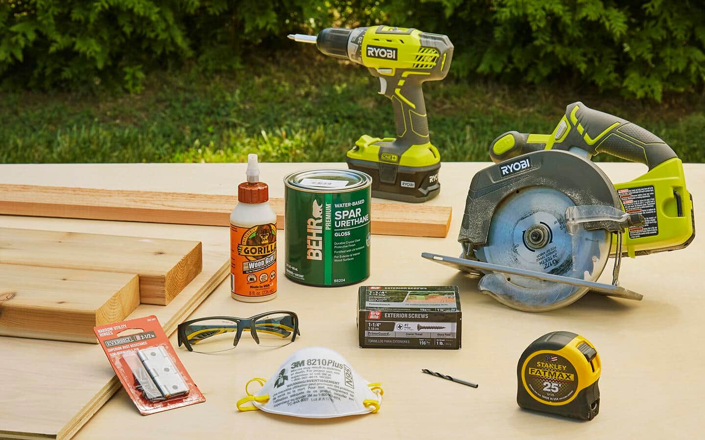 Building supplies including a power drill, screws, saw, tape measure and safety glasses on a table. Building supplies including a power drill, screws, saw, tape measure and safety glasses on a table.