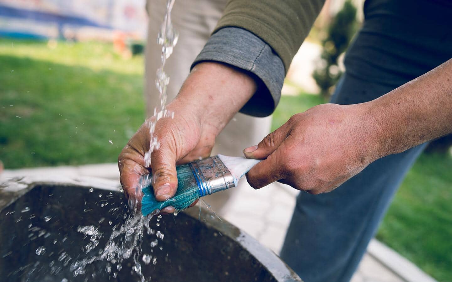 A person cleans off a paint brush using water. A person cleans off a paint brush using water.
