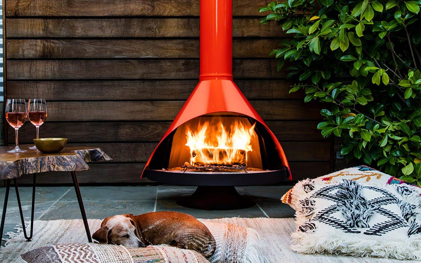 A dog resting on a rug in front of a woodstove with a fire