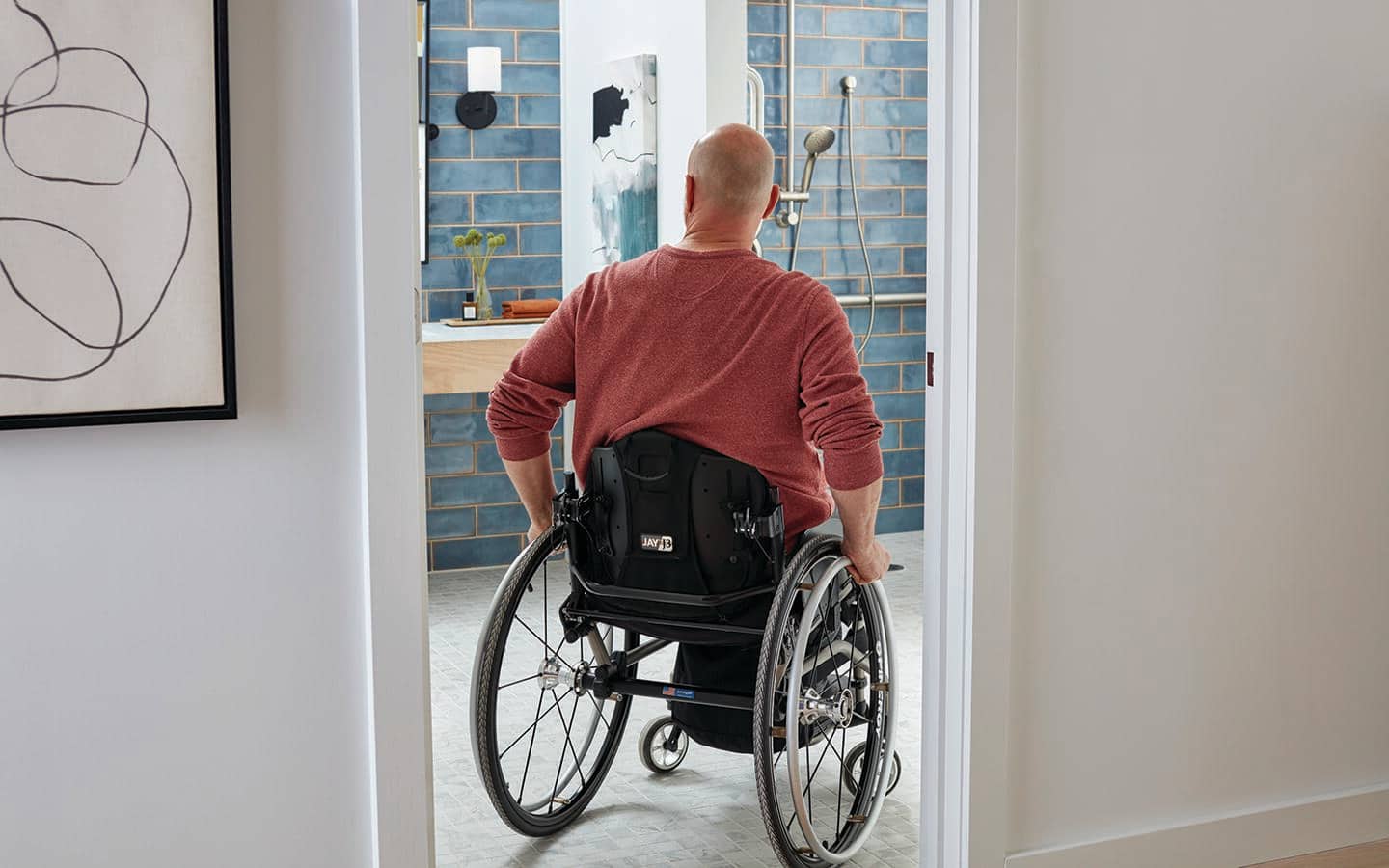 A person in a wheelchair enters an accessible bathroom through a doorway. A person in a wheelchair enters an accessible bathroom through a doorway.