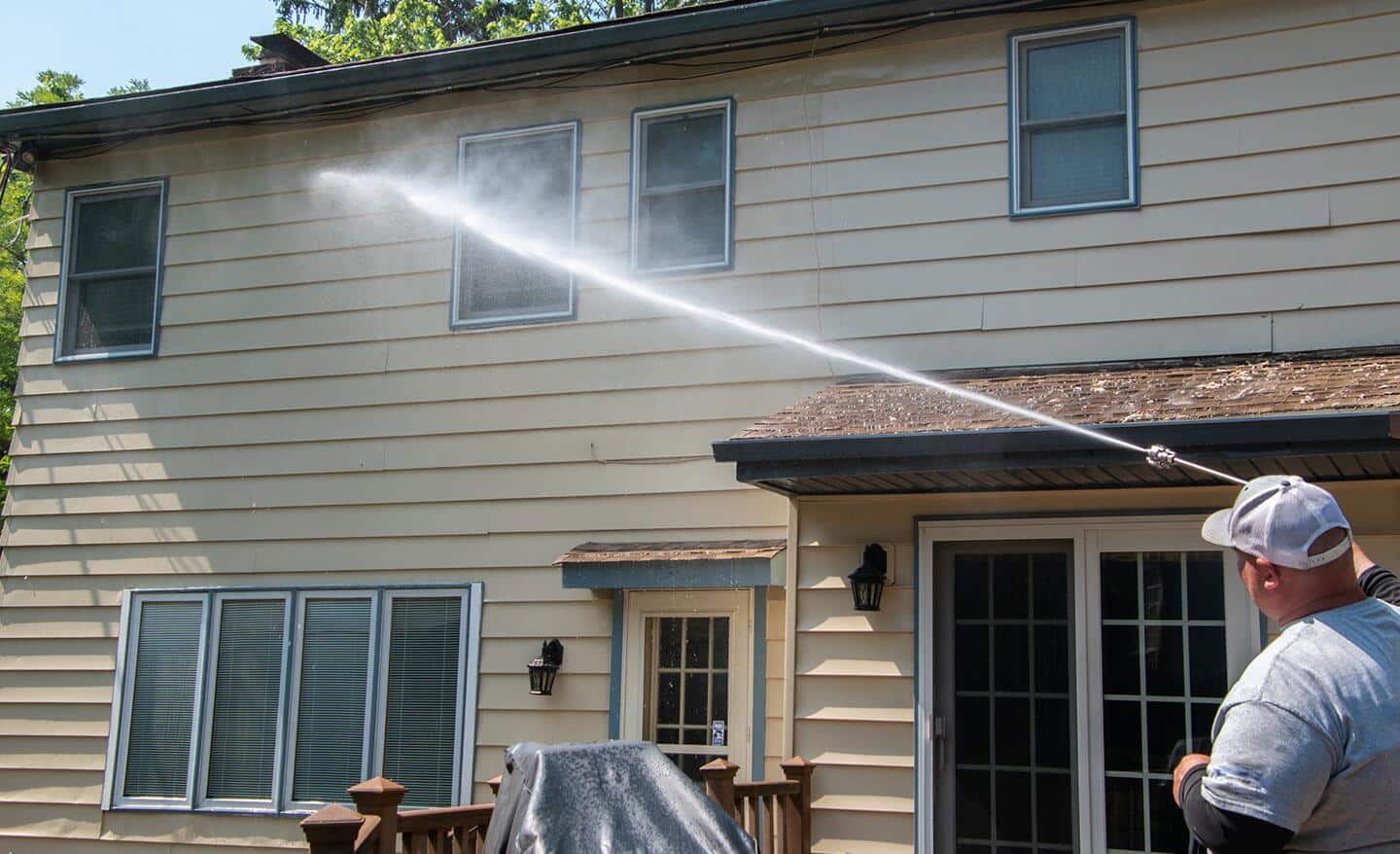 A man pressure washing the exterior of a home. A man pressure washing the exterior of a home.