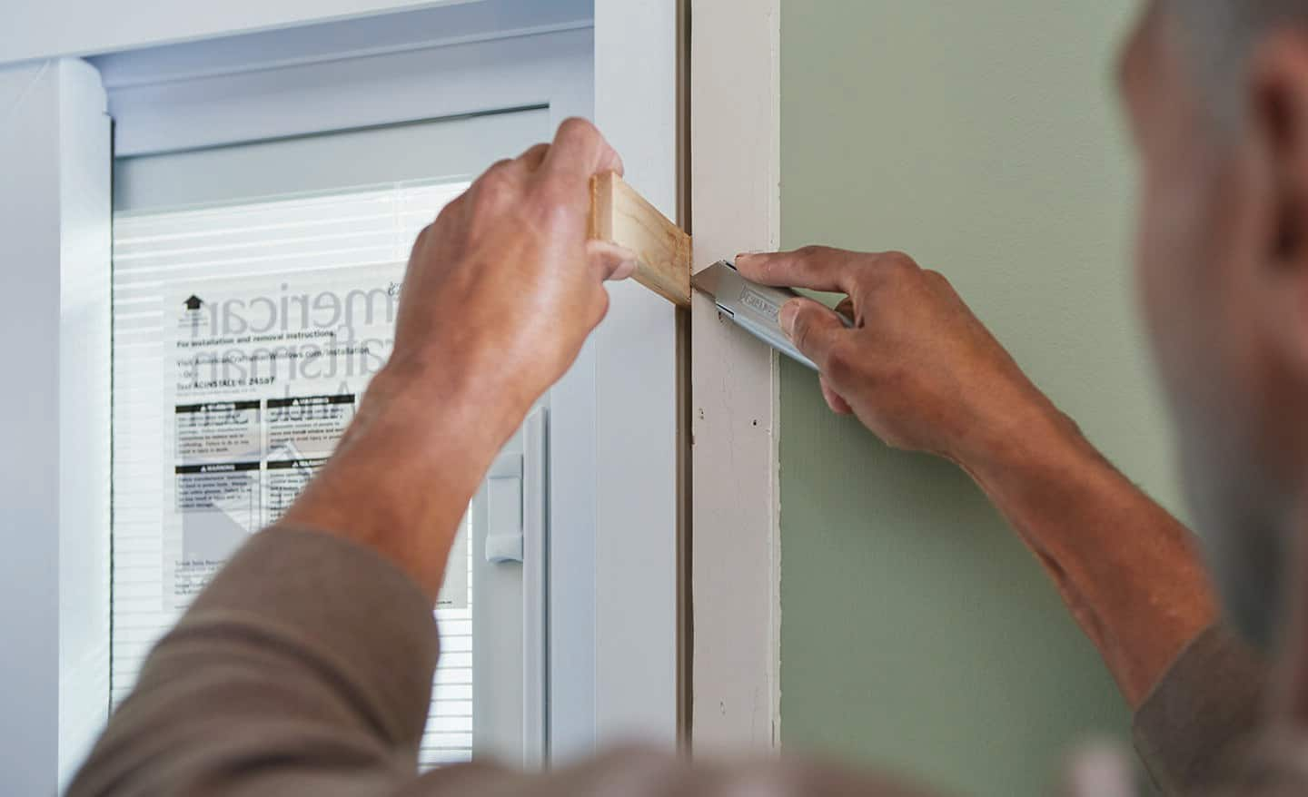 Someone scores a shim with a utility knife while securing a sliding door frame.