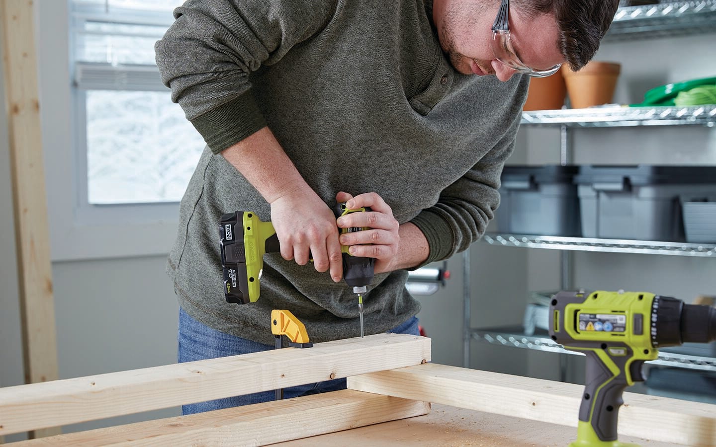 A man in a workshop using a cordless screwdriver to screw wooden board together. A man in a workshop using a cordless screwdriver to screw wooden board together.