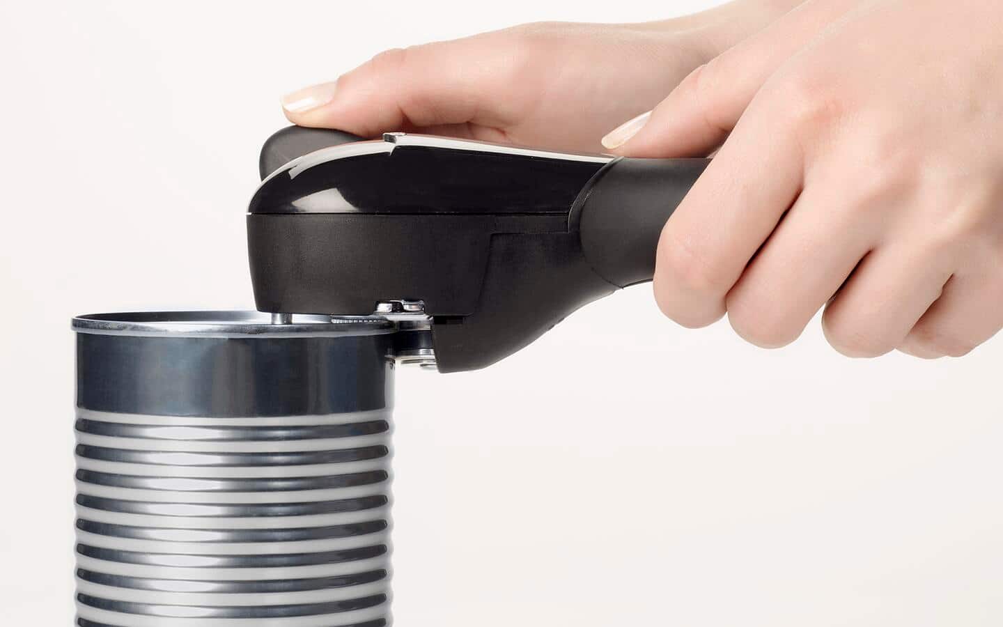Someone using a handheld can opener to open a can. Someone using a handheld can opener to open a can.