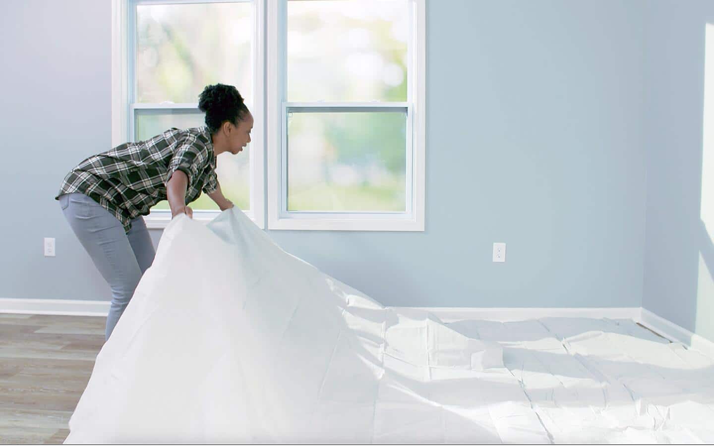 A person spreading drop cloths on a floor before painting. A person spreading drop cloths on a floor before painting.