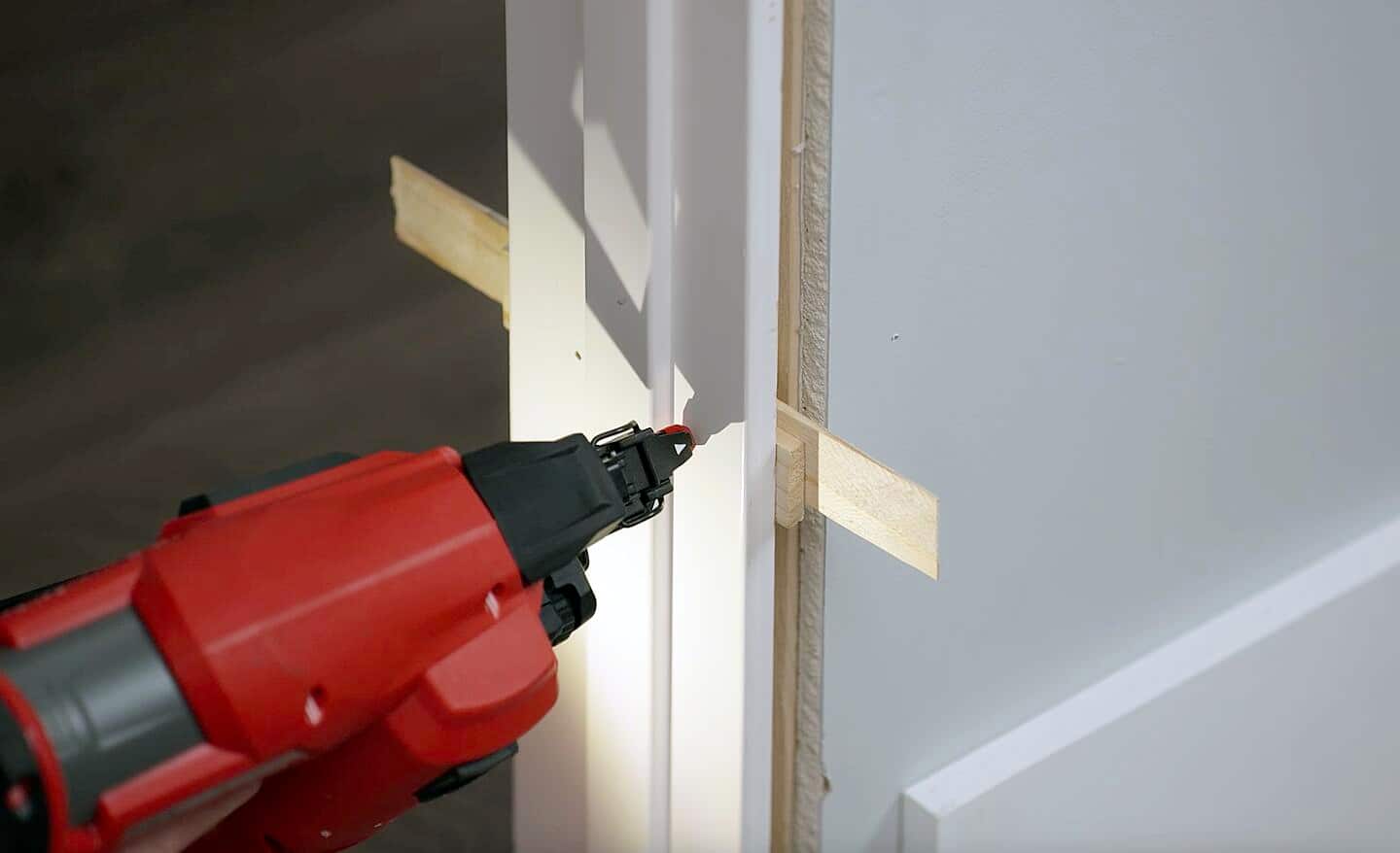 A person using a brad nailer to drive nails through a door frame into the wall.