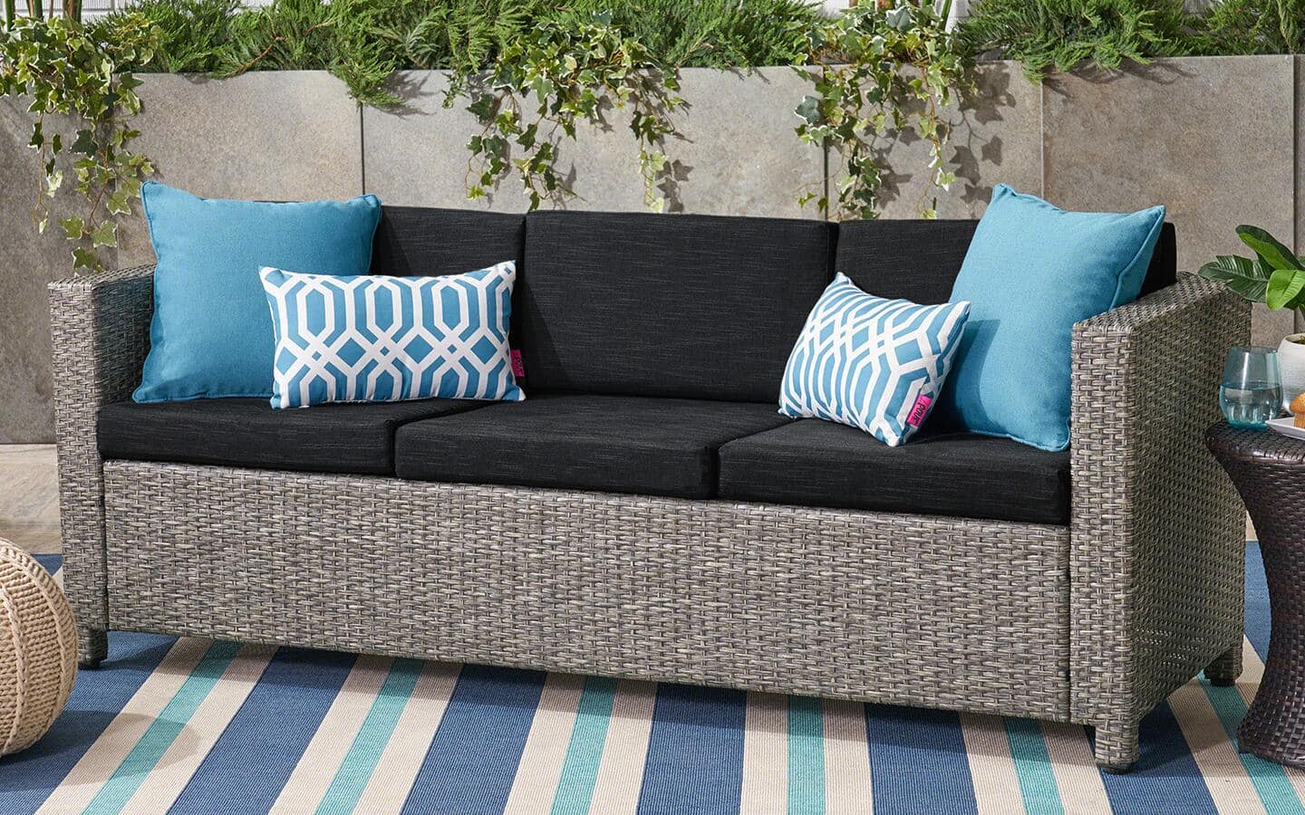 An outdoor sofa with blue pillows on an outdoor rug displayed on a patio in spring