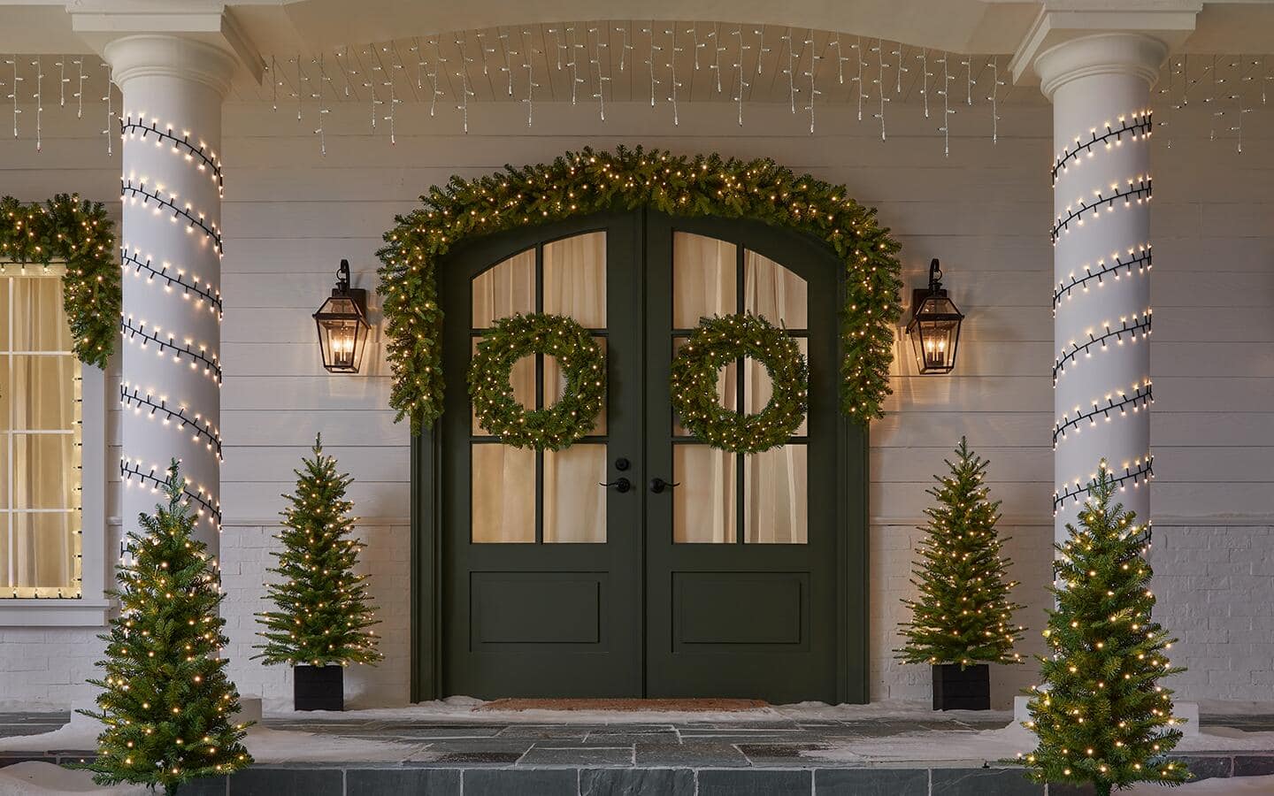 Double front doors beautifully decorated with lighted holiday garland, wreaths and front porch trees. Double front doors beautifully decorated with lighted holiday garland, wreaths and front porch trees.