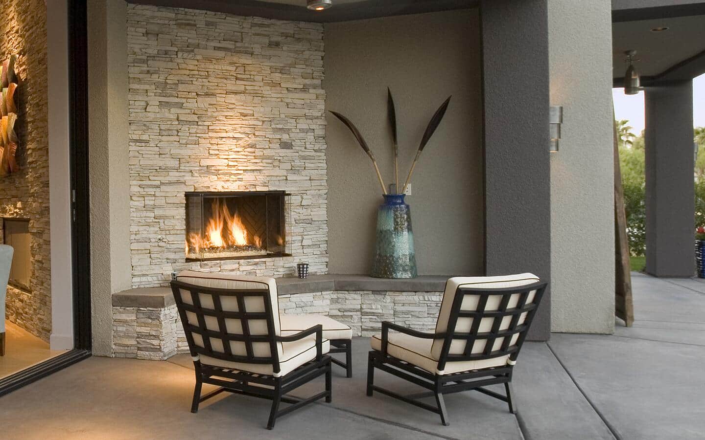 A covered patio with a modern outdoor fireplace and comfortable chairs.