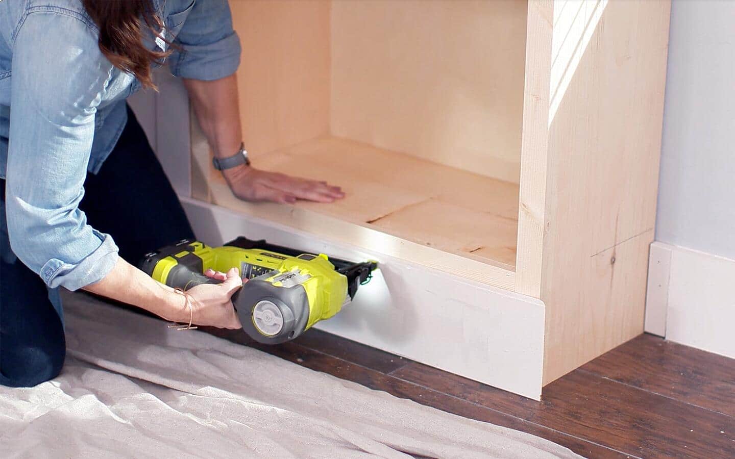A person installing a baseboard on a DIY bookshelf. A person installing a baseboard on a DIY bookshelf.