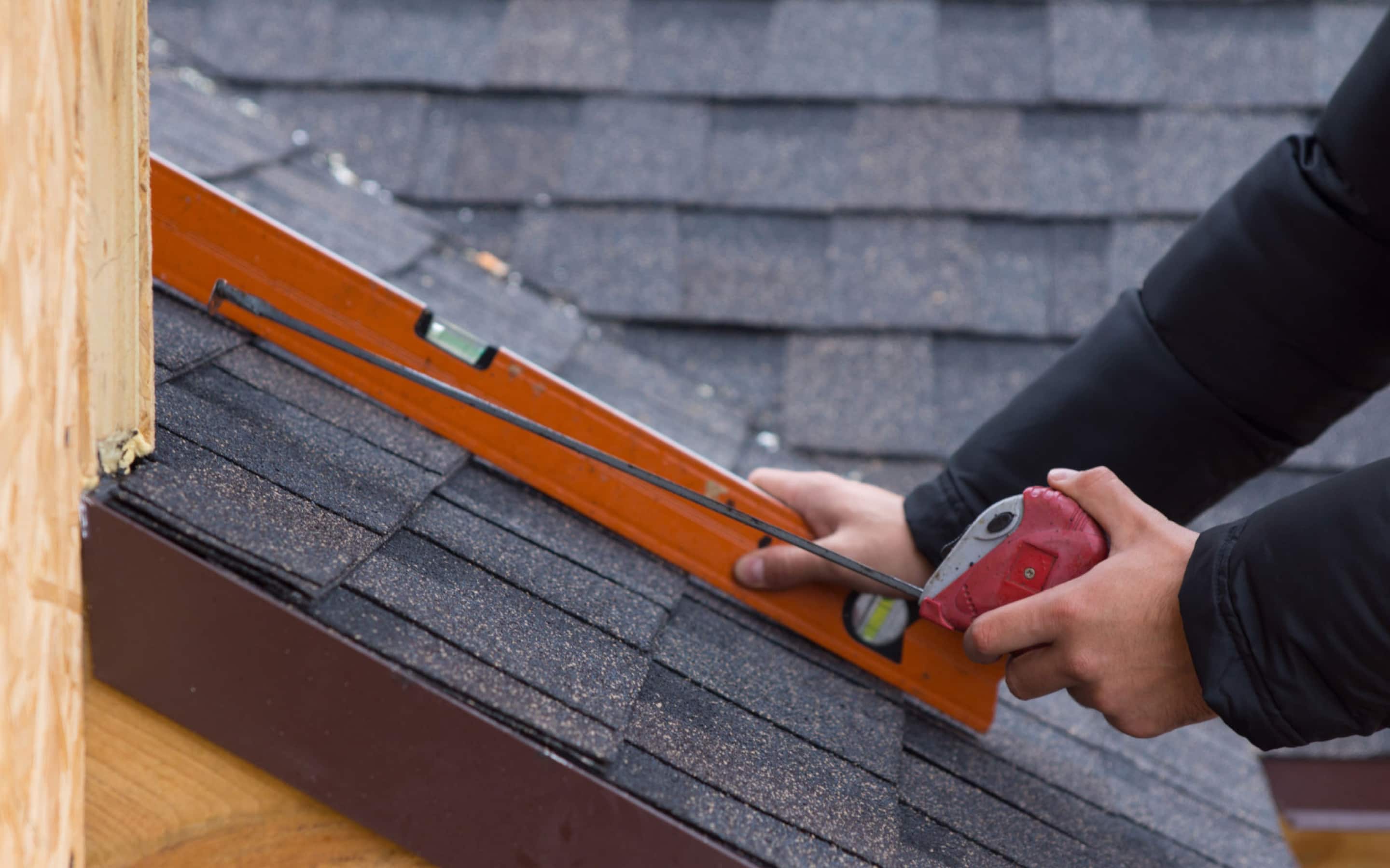 A contractor measures the roof's slope with a level over asphalt shingles.