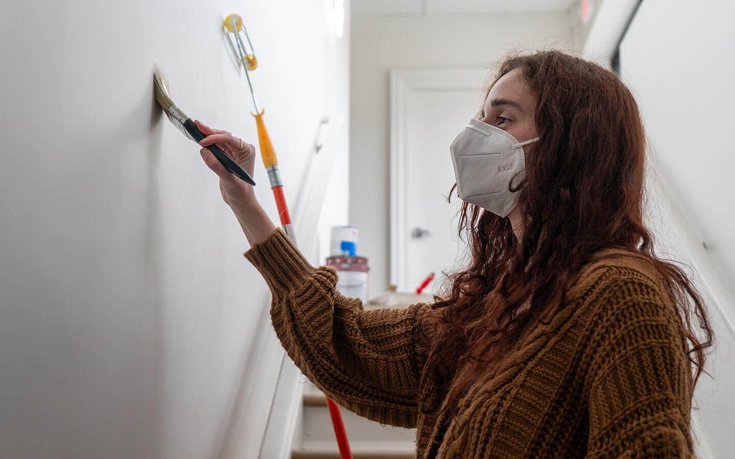 A woman wears a respirator while painting a wall. A woman wears a respirator while painting a wall.