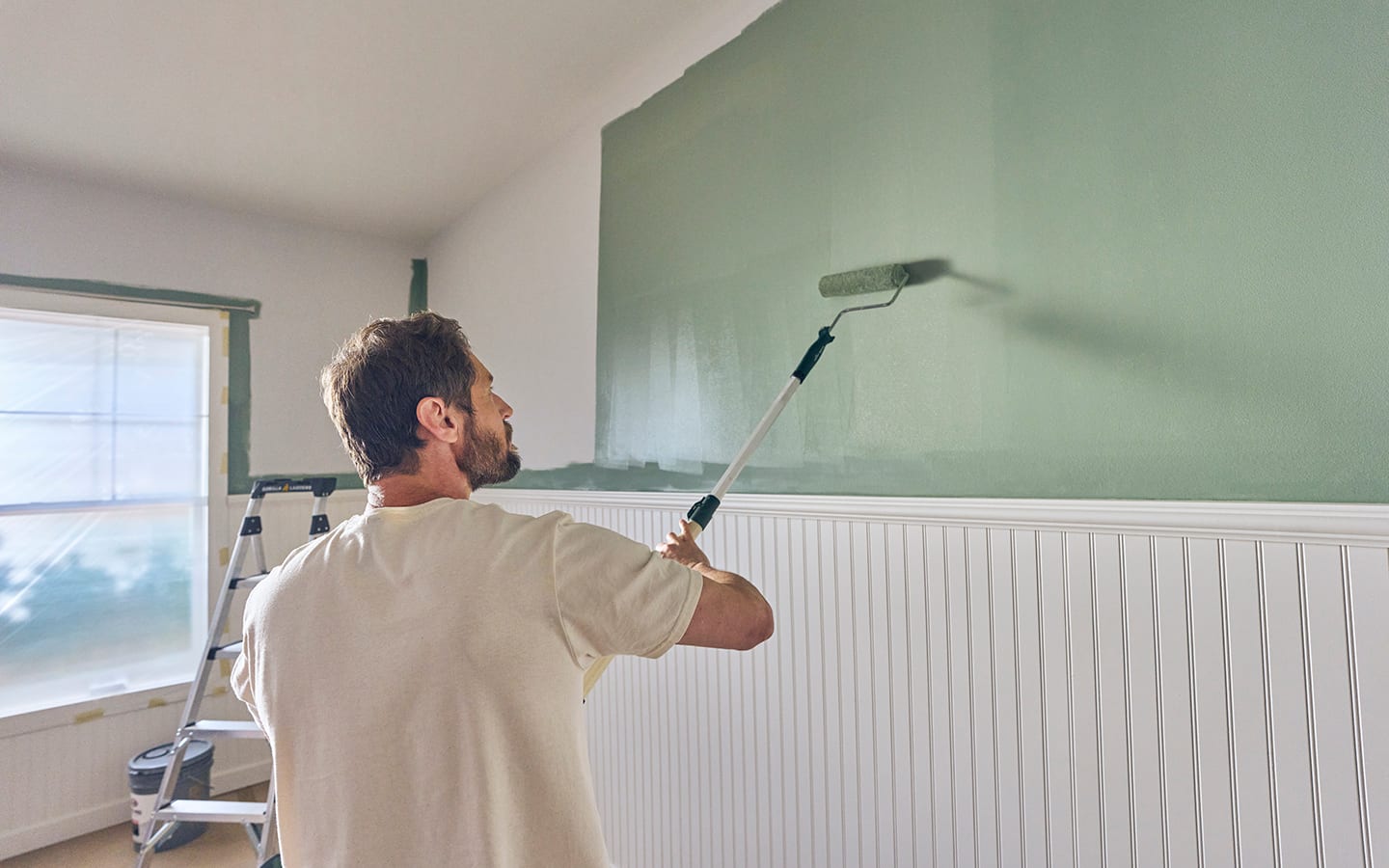 An individual applying green paint with a roller to an accent wall with mouldings. An individual applying green paint with a roller to an accent wall with mouldings.